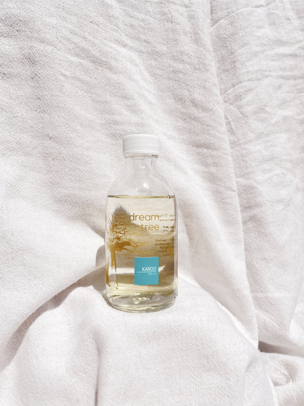 A 200ml clear glass diffuser refill bottle with a white cap, labeled 'Dream Tree' and 'Karooflora', placed on a white fabric background.